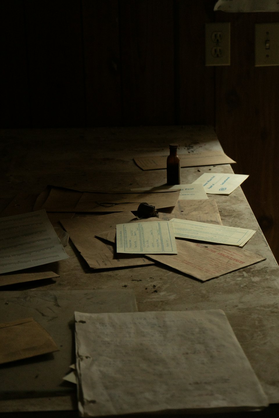 Carte e documenti sparsi su un tavolo di legno polveroso.